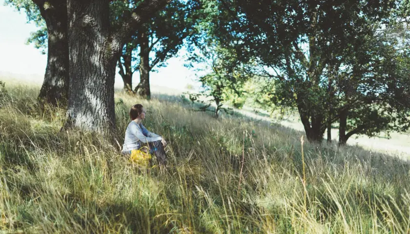 En person sitter i gräset under ett träd. Kanske en paus för att bajsa i skogen.