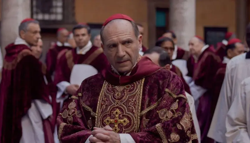 Scena z filmu o papieżu. Kardynał w bogato zdobionej szacie z czerwonym piuską. W tle inni duchowni.