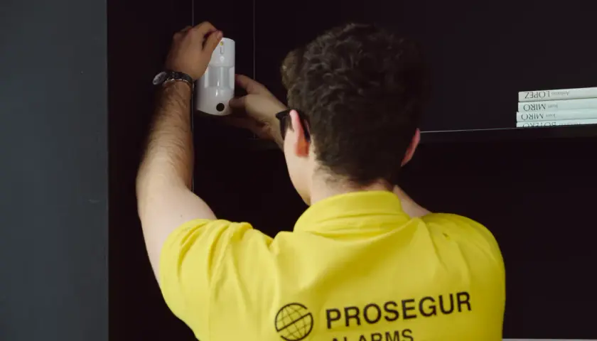 Técnico instala un sensor PIR blanco en una estantería, asegurando la protección del hogar.