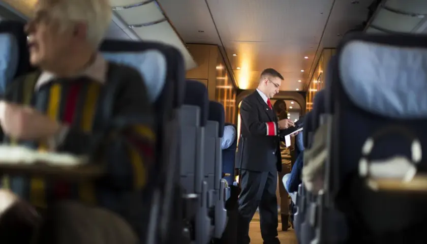 Ein Schaffner im deutschen Zugsystem prüft Tickets. Passagiere sitzen in den Reihen.