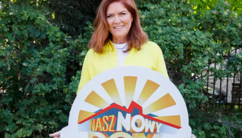 Katarzyna Dowbor z uśmiechem prezentuje tablicę z napisem "Nasz Nowy Dom".