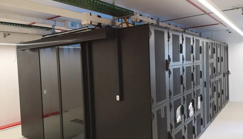Un micro data center avec des baies de serveurs noires et une porte vitrée. Des câbles et des conduits sont visibles au plafond.