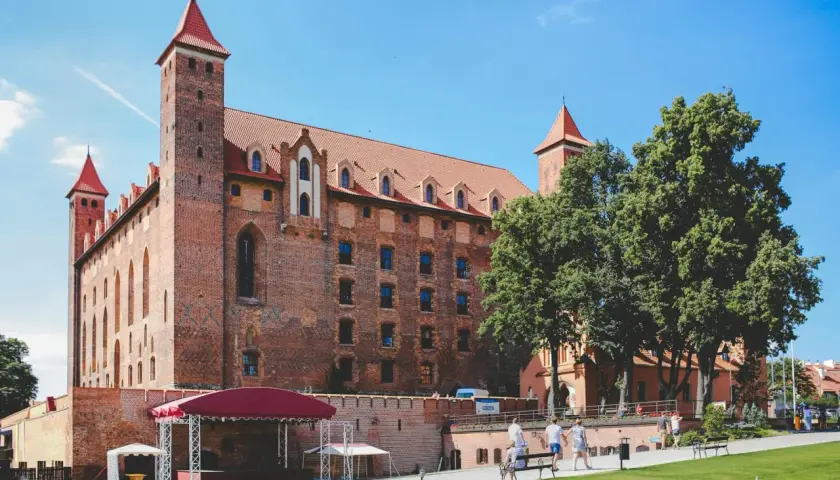 Zamek w Malborku, największe województwo w Polsce, z czerwonymi dachami i wieżami, otoczony zielenią i błękitnym niebem.