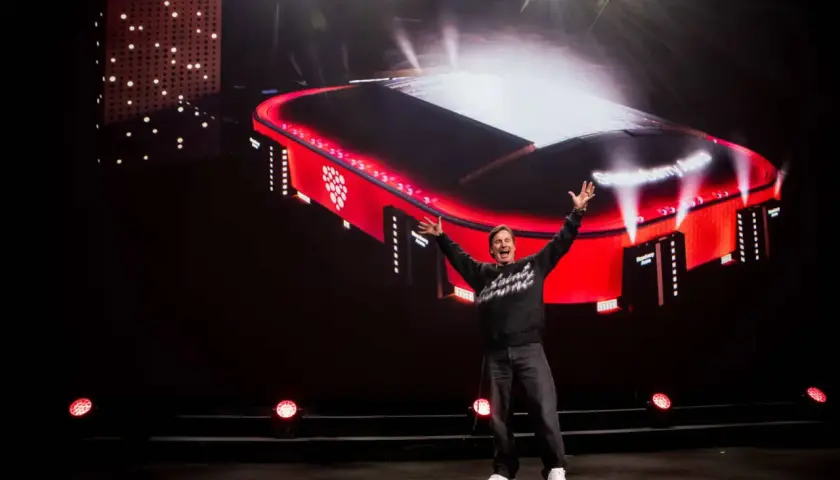 En man med armarna uppsträckta jublar framför en storbildsskärm som visar en röd arena med texten "Strawberry Arena".