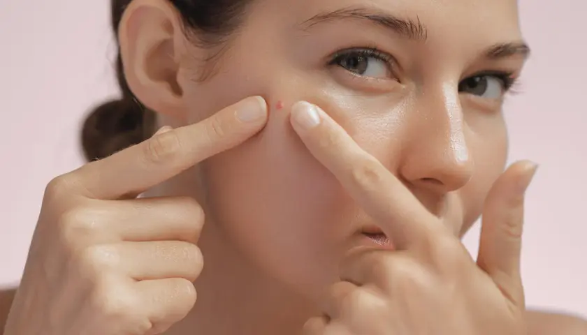 Une jeune femme examine un bouton sur sa joue, un signe possible pour savoir si on a une peau grasse.