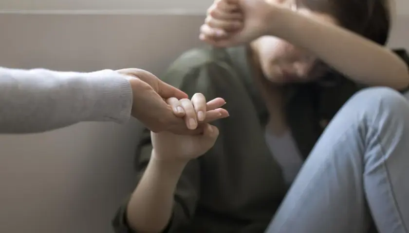 Dłoń wyciągnięta do osoby skulonej, zakrywającej twarz.