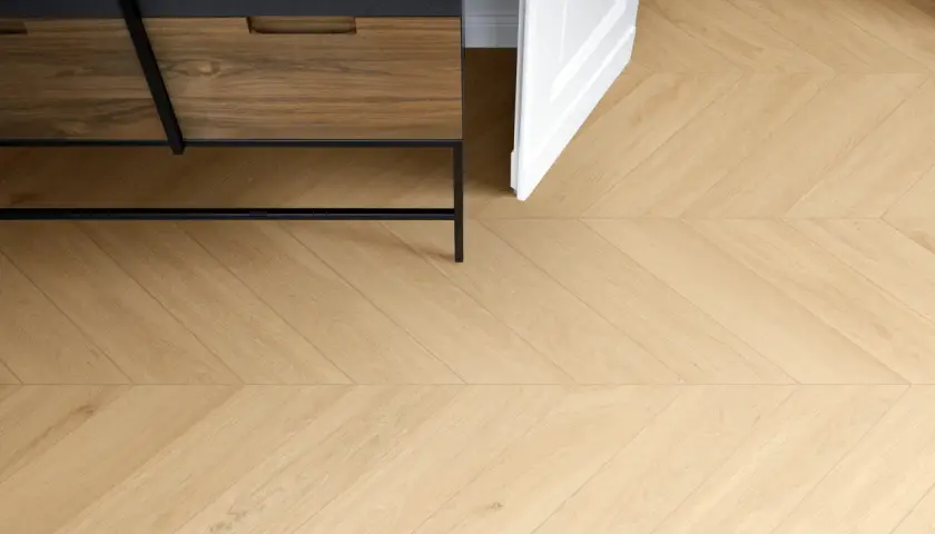 Posa di un elegante parquet in gres porcellanato effetto legno, con un motivo a spina di pesce che si estende verso una porta bianca aperta.