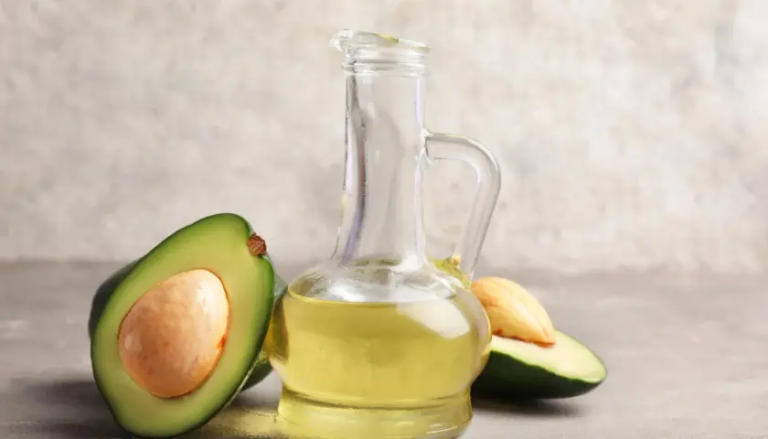 Bouteille en verre remplie d'huile avocat dorée, avec des moitiés d'avocat frais autour.