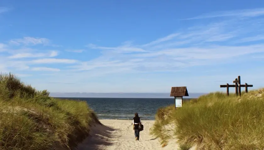 Kobieta idzie piaszczystą ścieżką na plażę. To idealne miejsce na chwilę wytchnienia podczas podróży samochodem.