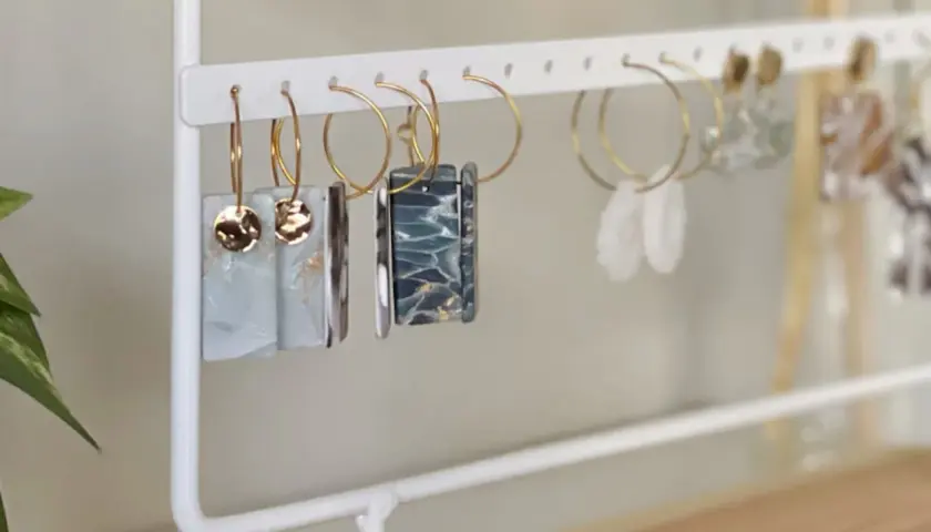 Un porta pendientes blanco exhibe varios pares de aretes colgantes, algunos con detalles dorados y otros con diseños marmoleados.