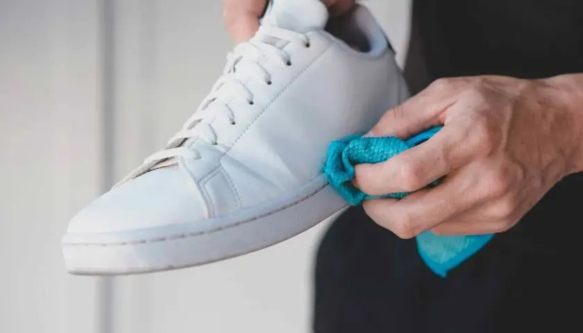 Manos limpiando las gomas de unas zapatillas blancas con un paño azul. Un detalle para saber como limpiar las gomas de las zapatillas y dejarlas como nuevas.