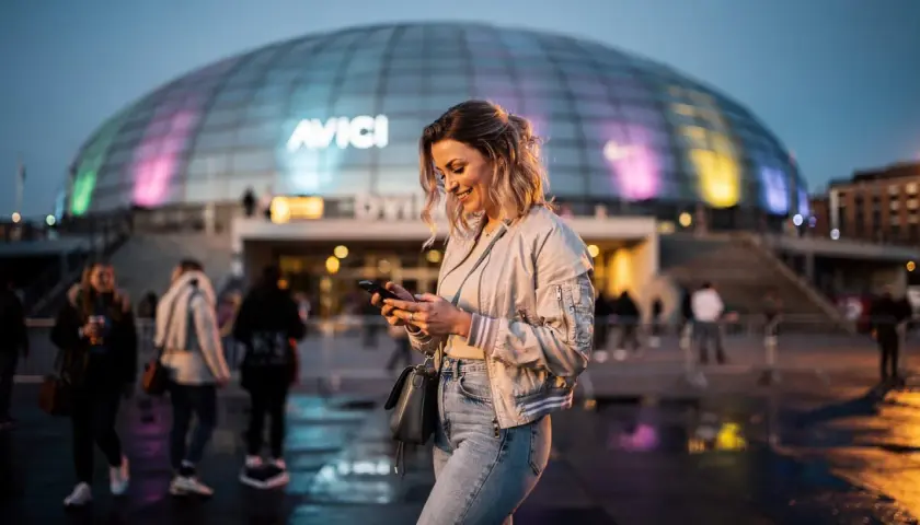 Glad kvinna med mobil framför Avicii Arena, Stockholm. Kanske väntar på en kyrkokonsert i Stockholm?