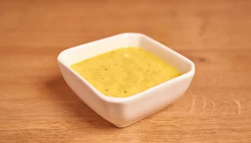 Un cuenco blanco contiene una cremosa salsa miel y mostaza, lista para acompañar tus platos.