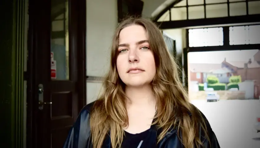 Miriam Ingrid, med sitt långa, vågiga hår och gröna ögon, blickar ut från en mörk port.