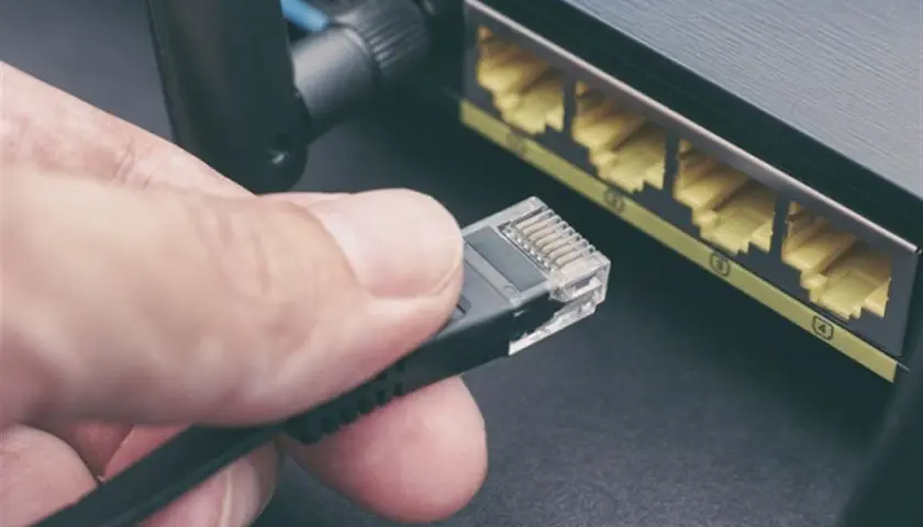 Main d'une personne tenant un câble rj45, prêt à le brancher dans un routeur. Connexion réseau.