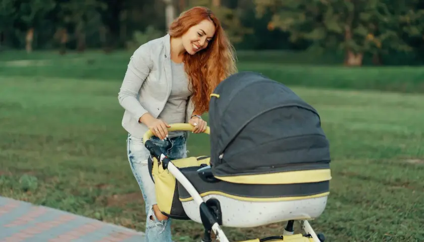 Uśmiechnięta mama z rudymi włosami przygotowuje się do spaceru, zastanawiając się, jak ubrać niemowlę na spacer.