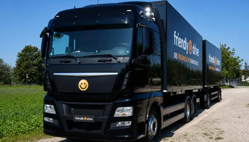 Schwarzer Lkw mit Anhänger, Werbung für "friendly drive - Die freundliche Fahrschule". Ein Smiley-Logo ziert die Front.