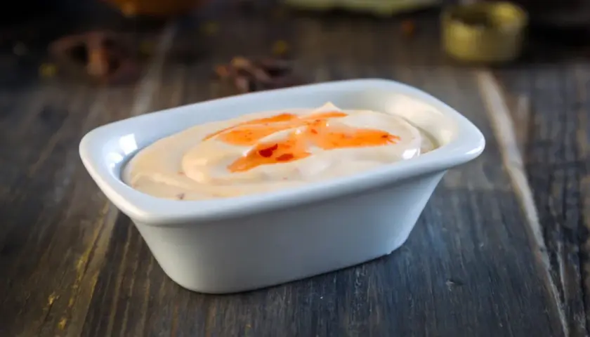 Krämig sås med en virvel av söt chili sås, serverad i en vit skål på en träyta.