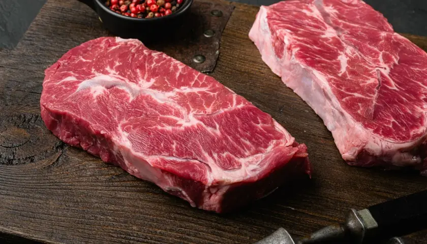 Deux beaux steaks de l angus beef, marbrés de gras, prêts à être cuisinés sur une planche en bois. Poivre rose en accompagnement.