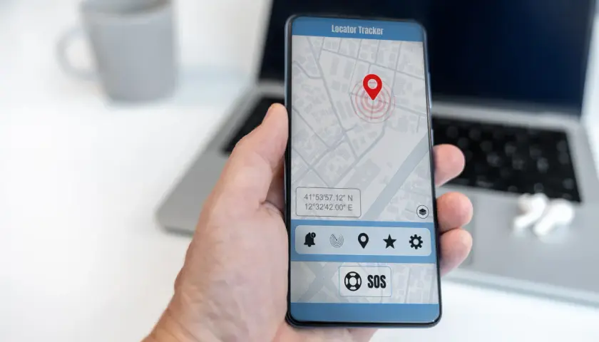 Dłoń trzyma smartfon z mapą i pinezką lokalizatora. To najlepsza darmowa aplikacja do śledzenia telefonu, z przyciskiem SOS.
