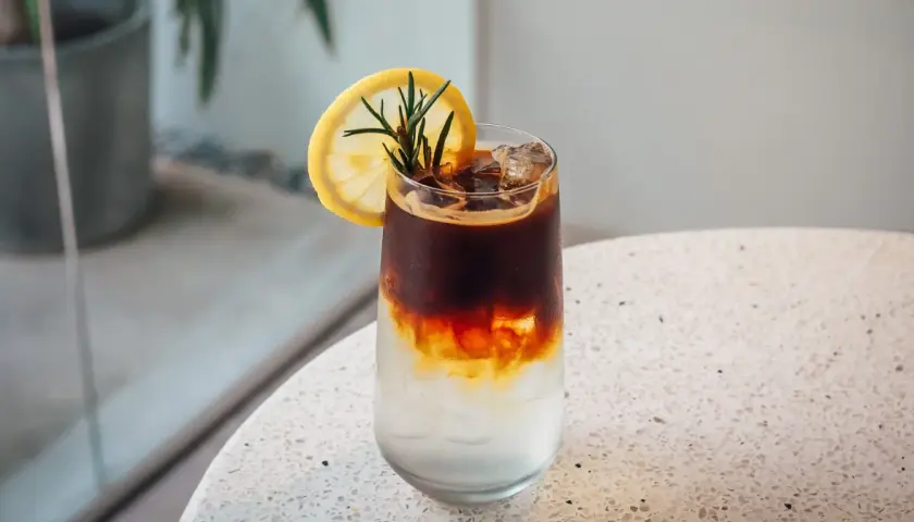 Orzeźwiający tonic espresso z plasterkiem cytryny i rozmarynem, idealny na upalny dzień.