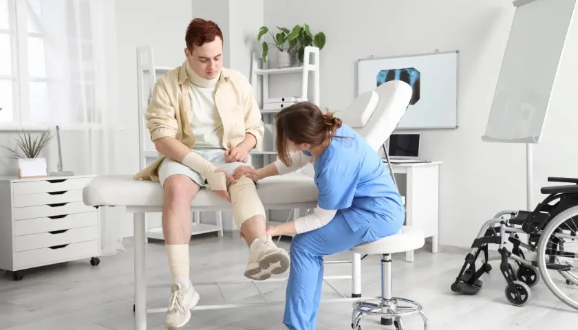 Fizjoterapeutka opatruje nogę pacjenta po urazie. Rehabilitacja pourazowa w gabinecie.