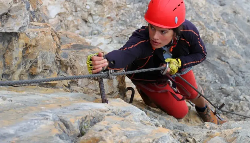 Młoda kobieta w kasku wspina się po skale, używając liny na via ferrata Czechy.