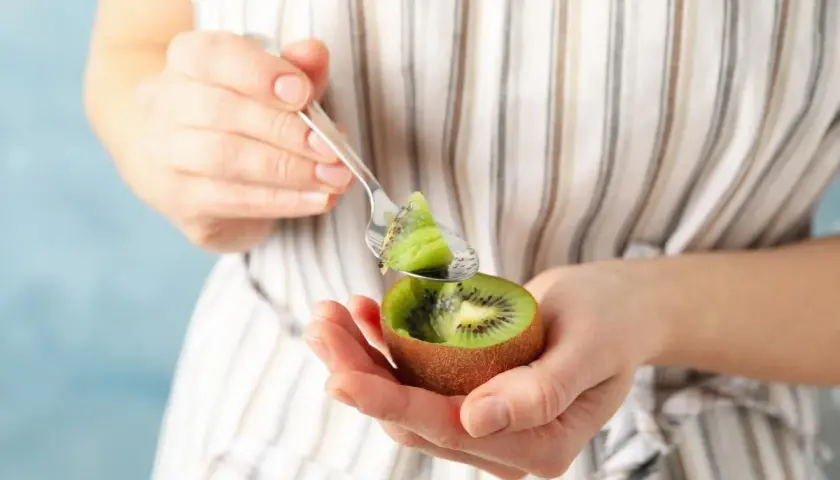 Kobieta trzyma w dłoniach połówkę kiwi i łyżeczkę z kawałkiem owocu.