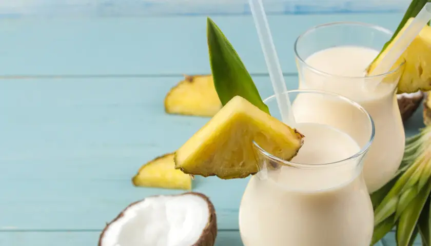 Dwa orzeźwiające koktajle pina colada z mlekiem, ozdobione kawałkami ananasa i liśćmi, na tle połówek kokosa.