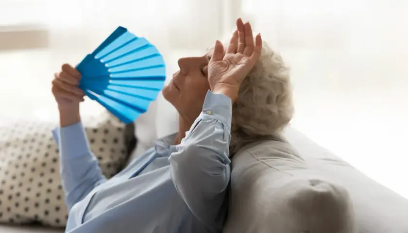 Une femme âgée s'évente avec un éventail bleu, montrant les effets de la chaleur sur les personnes âgées.