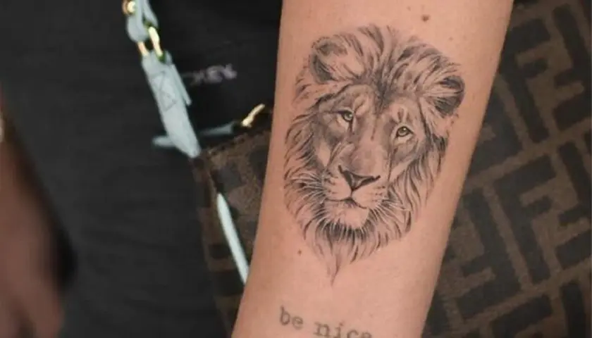 Tatuaż znak zodiaku lew na ramieniu, z napisem "be nice" poniżej.