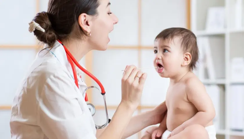 Medico esamina la gola di un bambino con abbassalingua, controllando sintomi di laringite bambini.