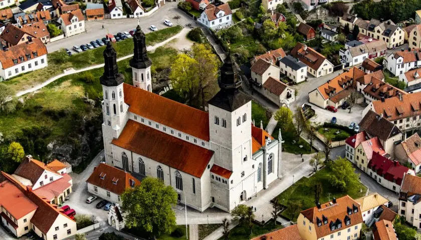 Widok z lotu ptaka na katedrę w Visby, otoczoną zabytkowymi budynkami z czerwonymi dachami.