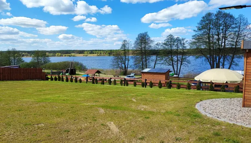 Piękny dzień nad jeziorem skarlińskim. Błękitne niebo z białymi chmurami, zielona trawa i spokojna tafla wody.