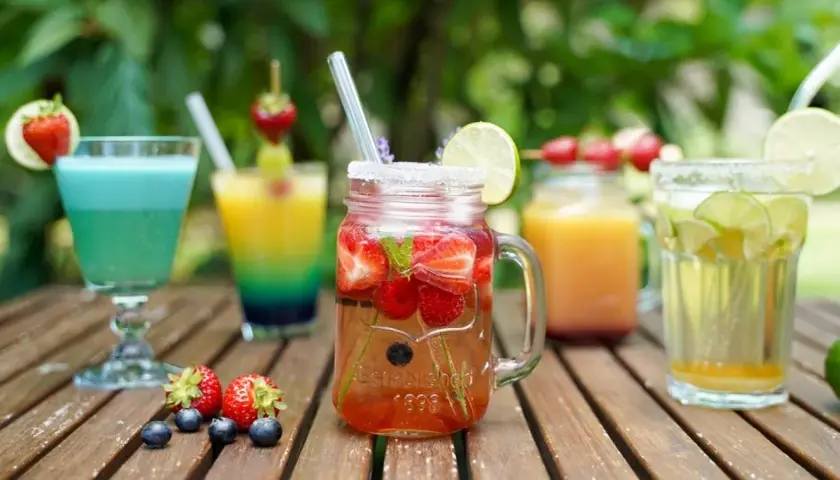 Erfrischende bunte Cocktails mit Früchten und Limette auf einer Holzoberfläche, perfekt für einen Sommertag.