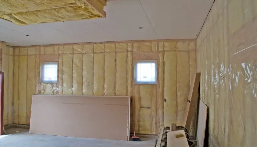 Travaux en cours pour isoler un garage non chauffé. Isolation jaune visible sur les murs et le plafond, avec des plaques de plâtre et des fenêtres.