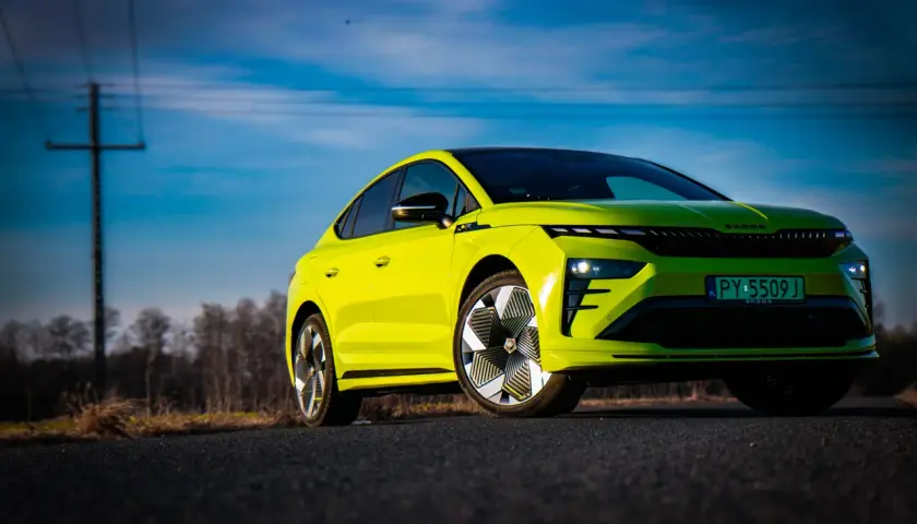 Jaskrawozielony Skoda Enyaq Coupe na tle błękitnego nieba z chmurami i linią energetyczną.