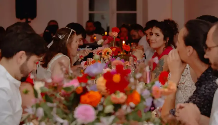 Des invités souriants partagent un repas de mariage festif, entourés de fleurs colorées. La durée du repas semble agréable.