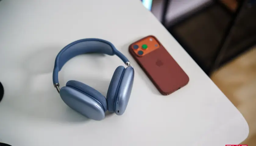 Niebieskie słuchawki AirPods Max i brązowy iPhone na białym biurku. Dowiedz się, jak połączyć AirPods z PC.