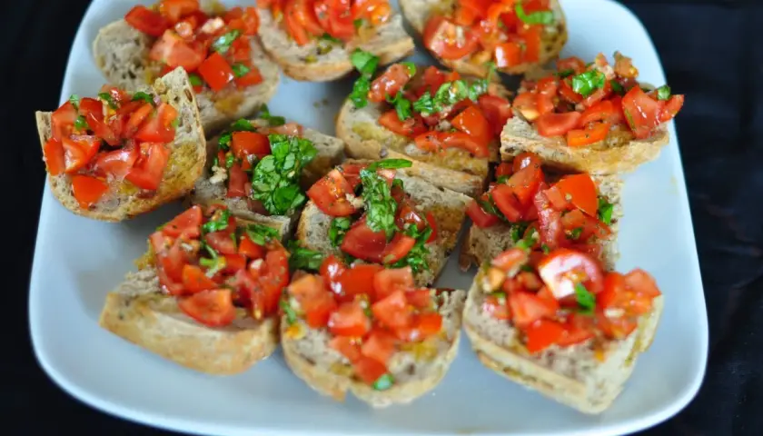 Bruschetta z pomidorami i bazylią, ułożona na białym talerzu. Chrupiące grzanki z dodatkiem świeżych, soczystych pomidorów i aromatycznej bazylii.