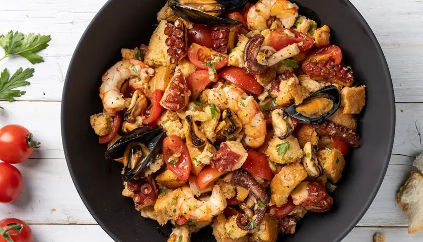 Panzanella di mare ricca con gamberi, polpo, cozze e pomodori, condita con pane raffermo. Un piatto estivo saporito.