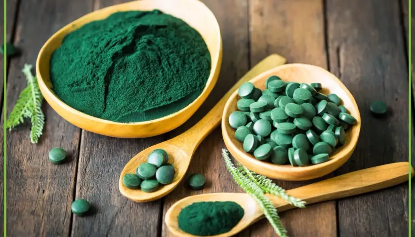 Zielona spirulina w proszku i tabletkach na drewnianym tle. Dowiedz się, spirulina co to jest i jakie ma właściwości.