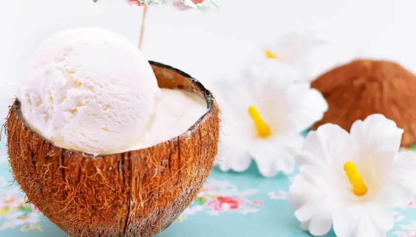 Delicioso helado de coco servido en su cáscara, adornado con una sombrilla tropical y flores blancas.