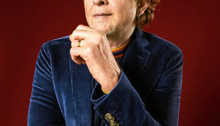 Mężczyzna z rudymi włosami, w granatowej sztruksowej marynarce, z dłonią na brodzie. To wokalista Simply Red.