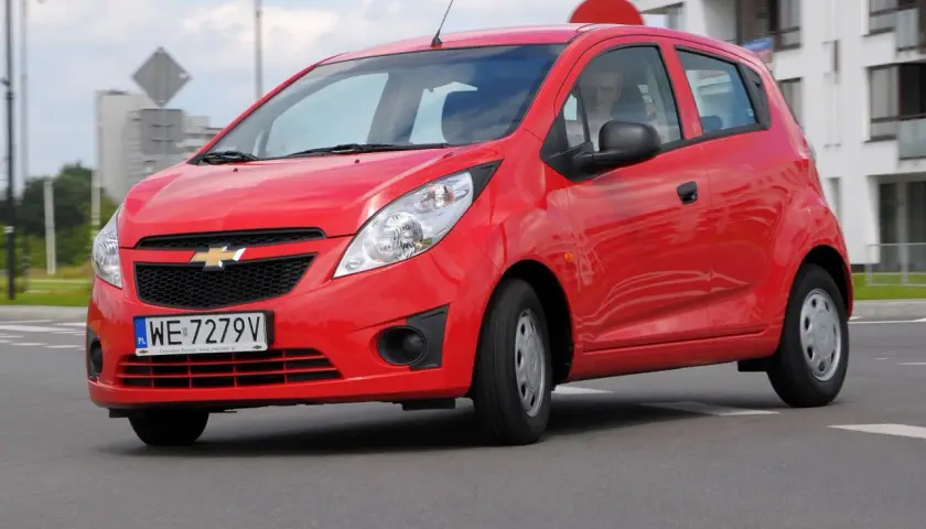 Czerwony Chevrolet Spark na drodze. Kierowca w środku. Wiele osób szuka chevrolet spark opinie przed zakupem.