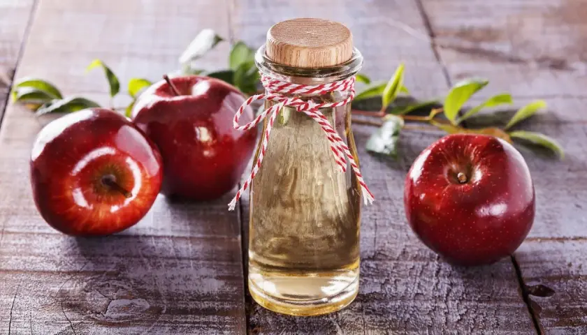 Rote Äpfel und eine Flasche Apfelessig auf Holz. Die natürliche Apfelessig Wirkung auf die Haut ist ein Geheimnis der Schönheit.