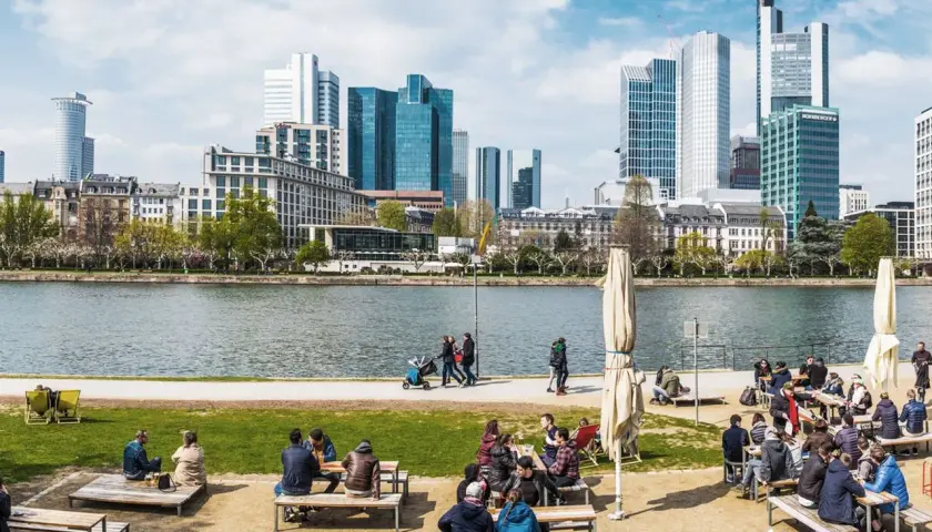 Frankfurt Geheimtipps: Menschen genießen das Leben am Mainufer mit Blick auf die Skyline. Ein perfekter Ort zum Entspannen und Beobachten.