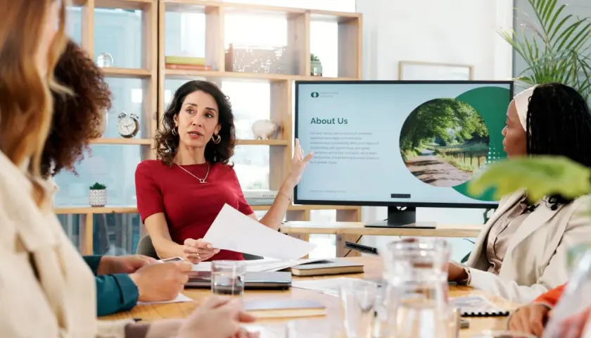 Kobieta tłumaczy, jak połączyć prezentacje powerpoint, wskazując na ekran z informacjami o firmie.