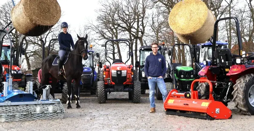 Ein Mann und eine Frau mit einem Pferd stehen vor mehreren Traktoren. Ein kleiner forsttraktor ist im Vordergrund zu sehen.