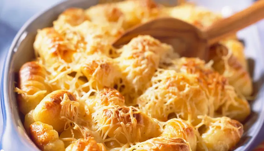 Un plat de gratin de gnocchi doré et gratiné au fromage, prêt à être servi avec une cuillère en bois.
